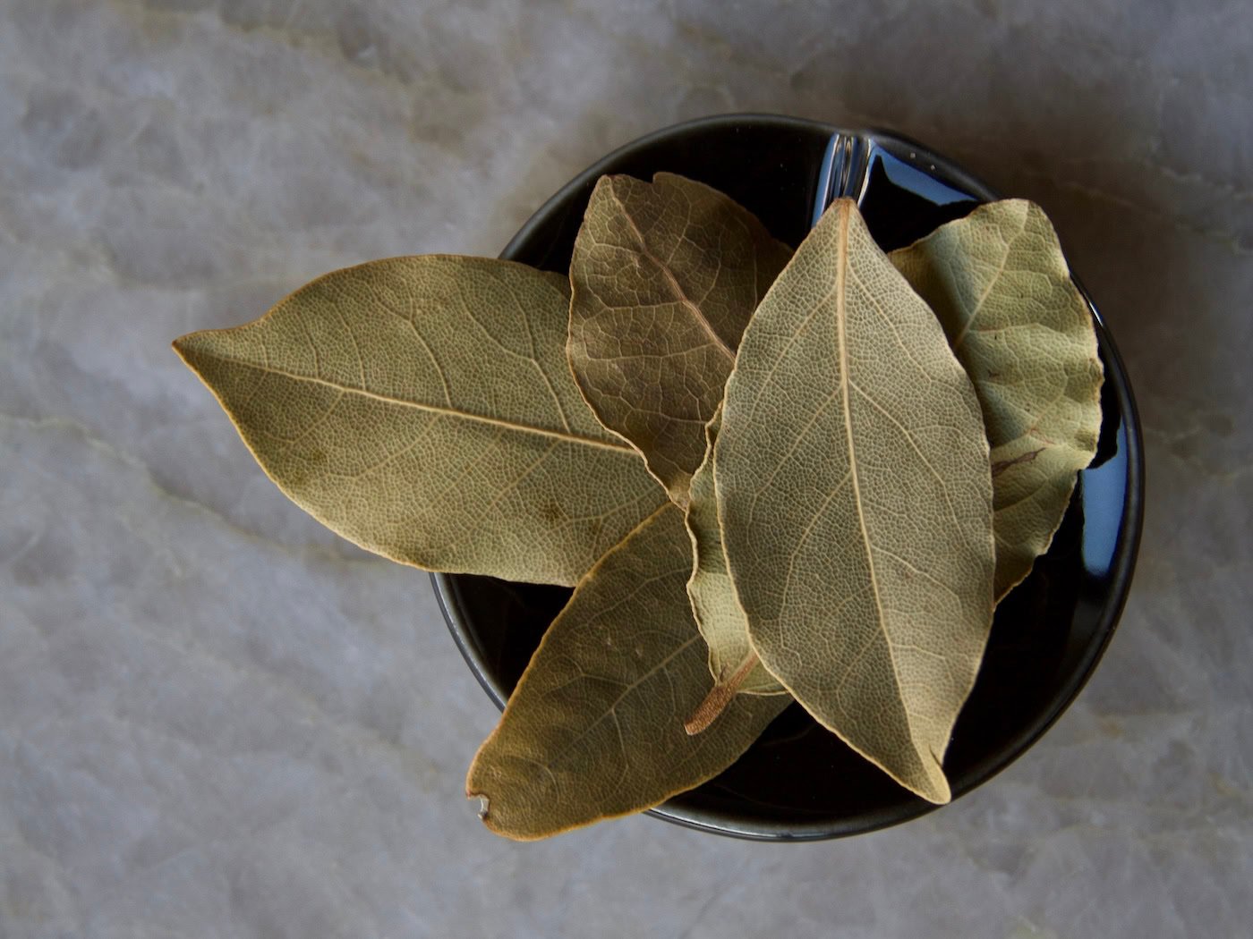 Bay leaves in black bowl on quartz