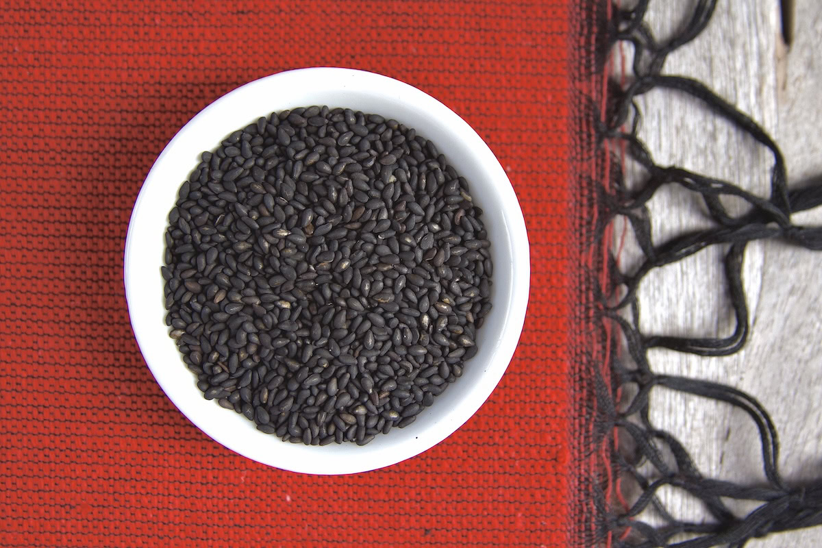 Black sesame seeds in a white bowl on red fabric
