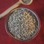 Fennel seed in ceramic bowl with spoon in background