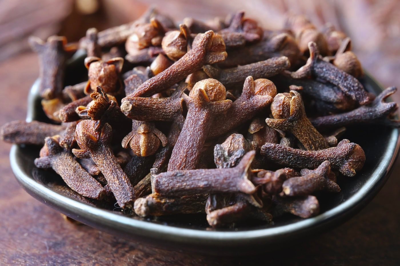 Clove buds in black bowl on wooden table