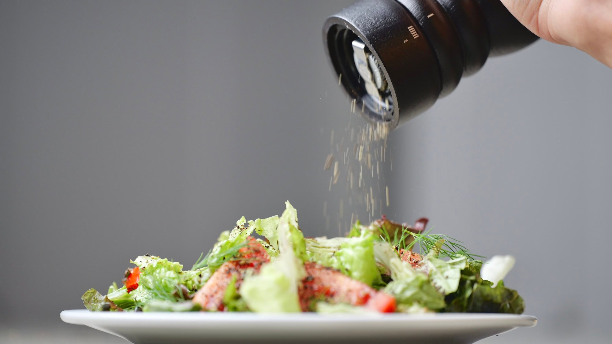 Cracking black peppercorns over a fresh salad