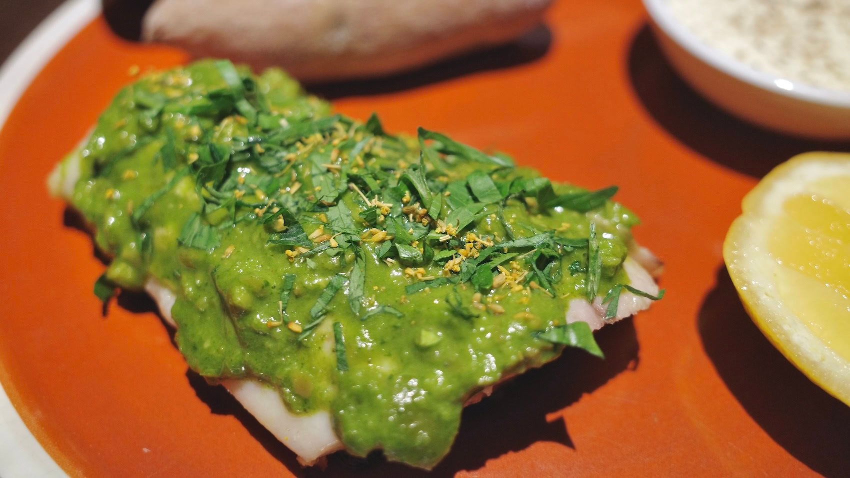 Seabass Salsa Verde with Sweet Basil and Fennel Pollen on brick red table with a lemon on the side