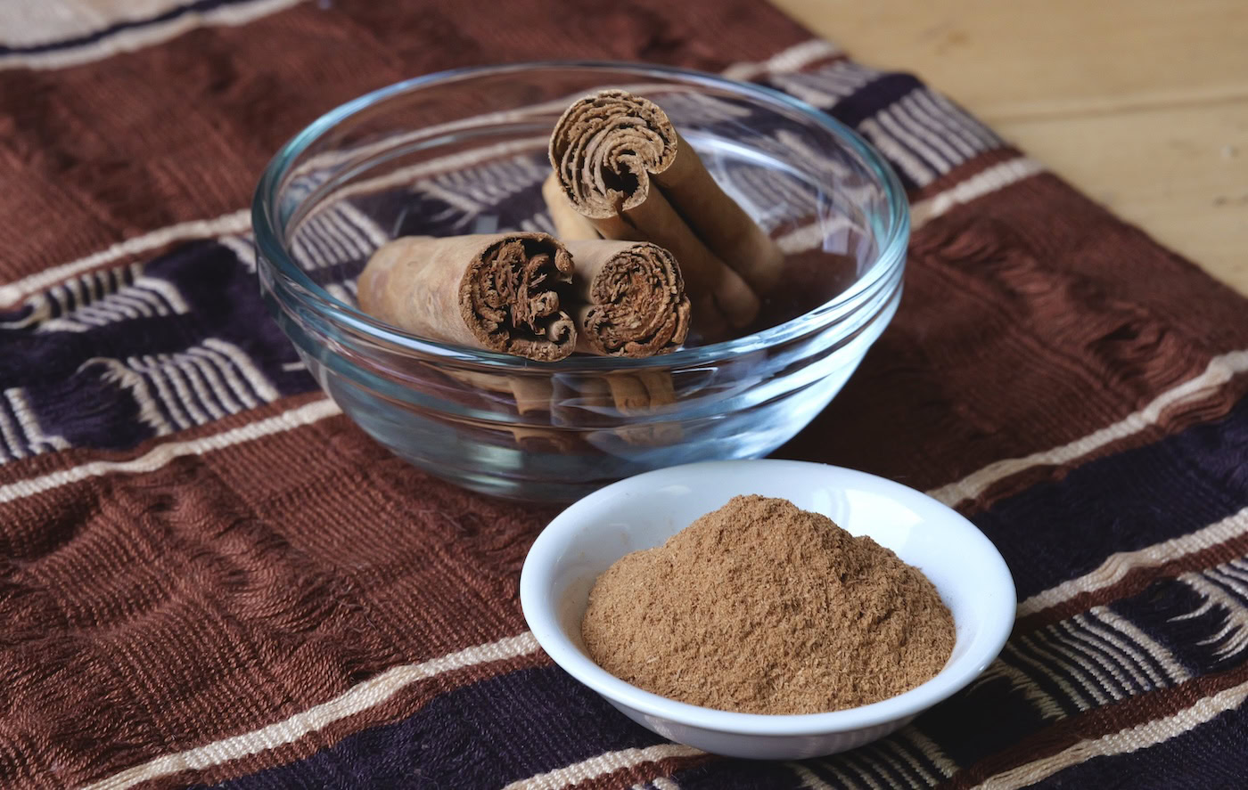 True cinnamon, whole and powdered against a beautiful patterned fabric
