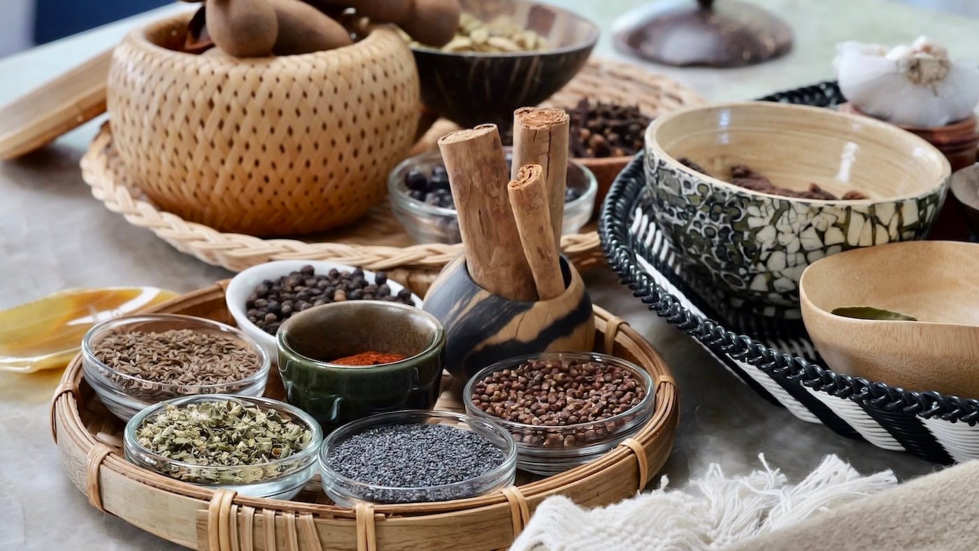 A table with many types of spices and herbs in a variety of vessels — bowls, cups, glasses, and trays.