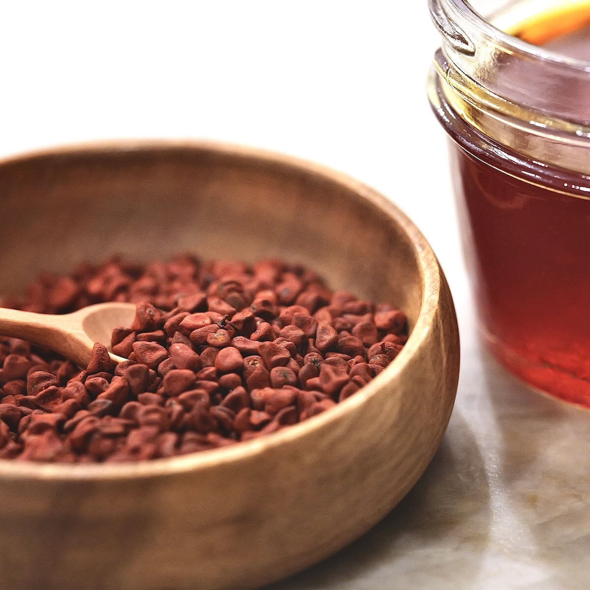 Annatto seeds in wooden bowl next to a glass jar of achiote oil