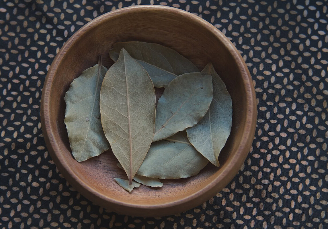 Bay leaves in wooden bowl on patterned fabric