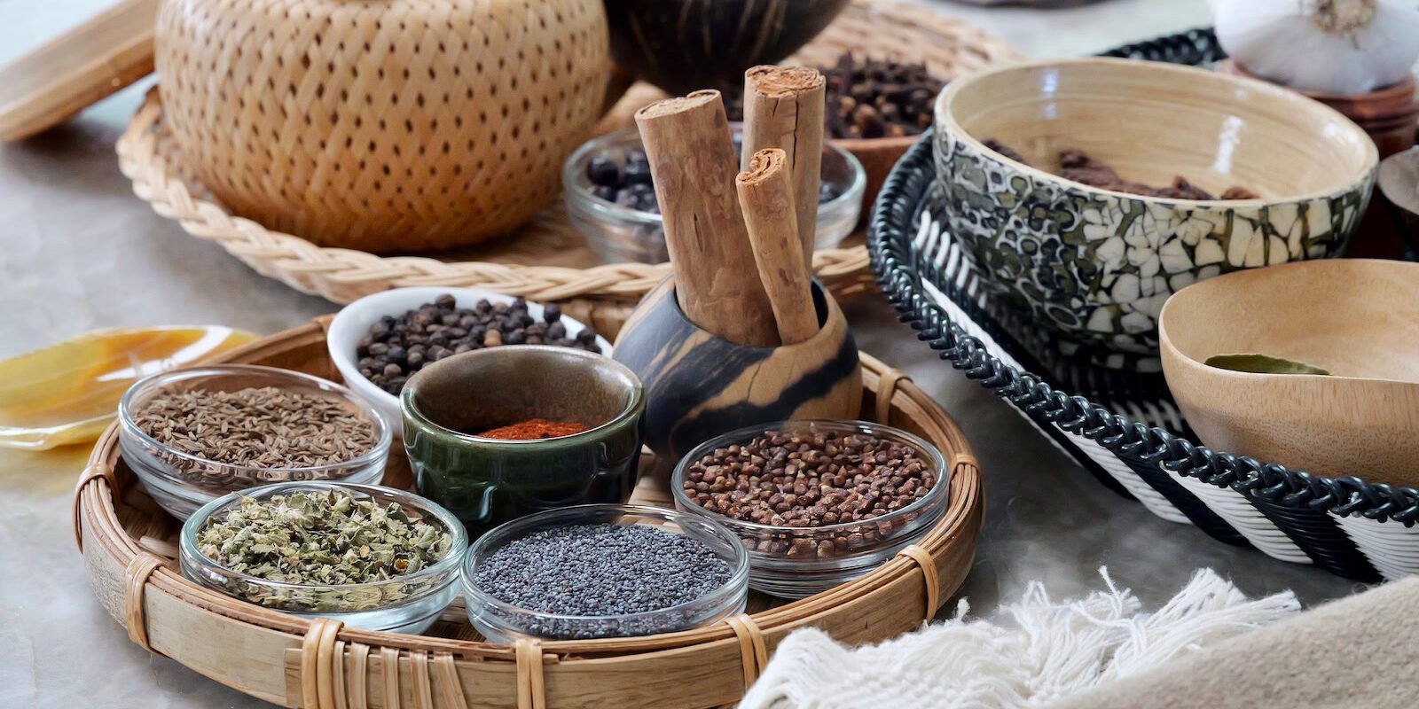 A table with many types of spices and herbs in a variety of vessels—bowls, cups, glasses, and trays.