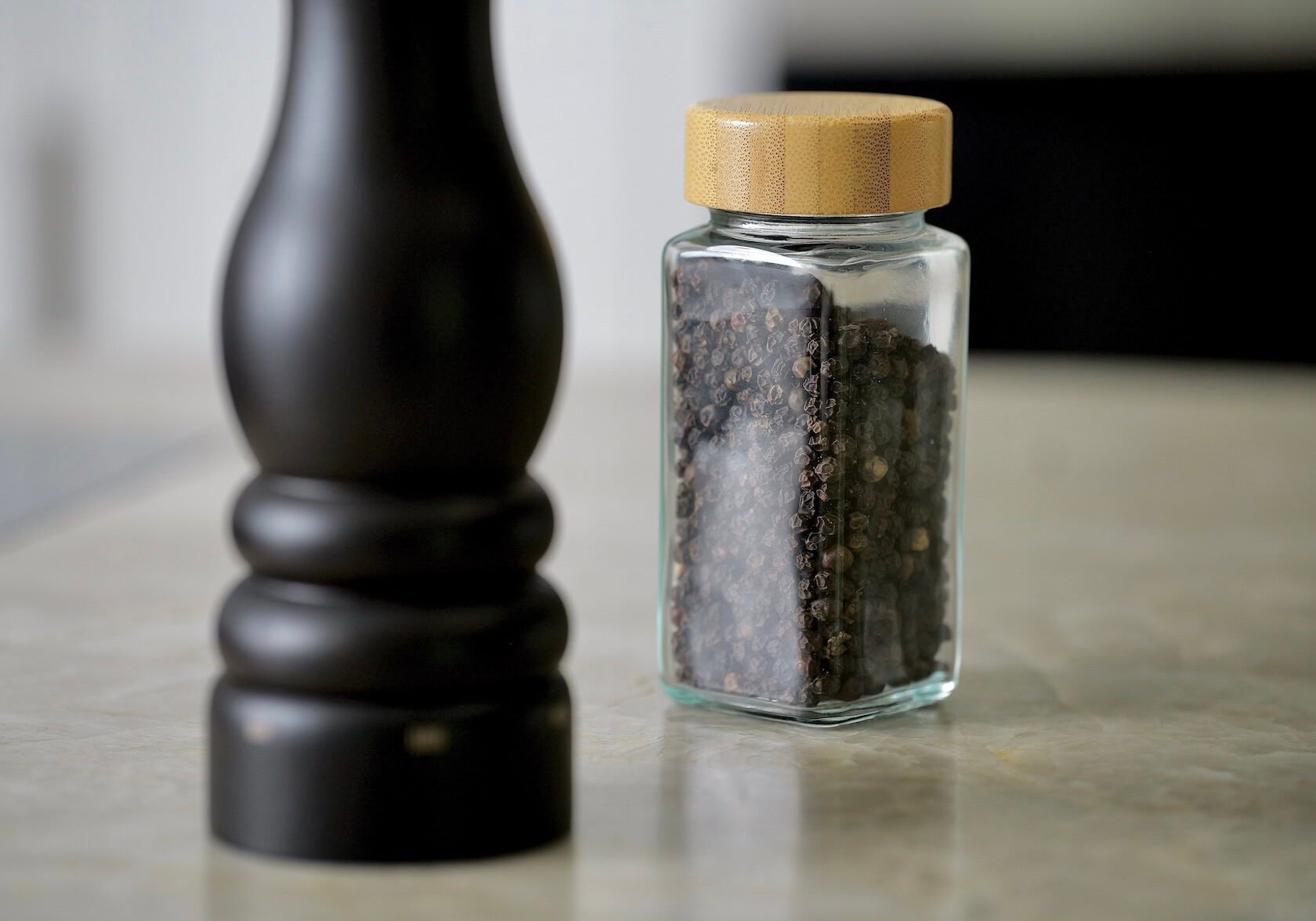 Black pepper in glass jar next to pepper mill