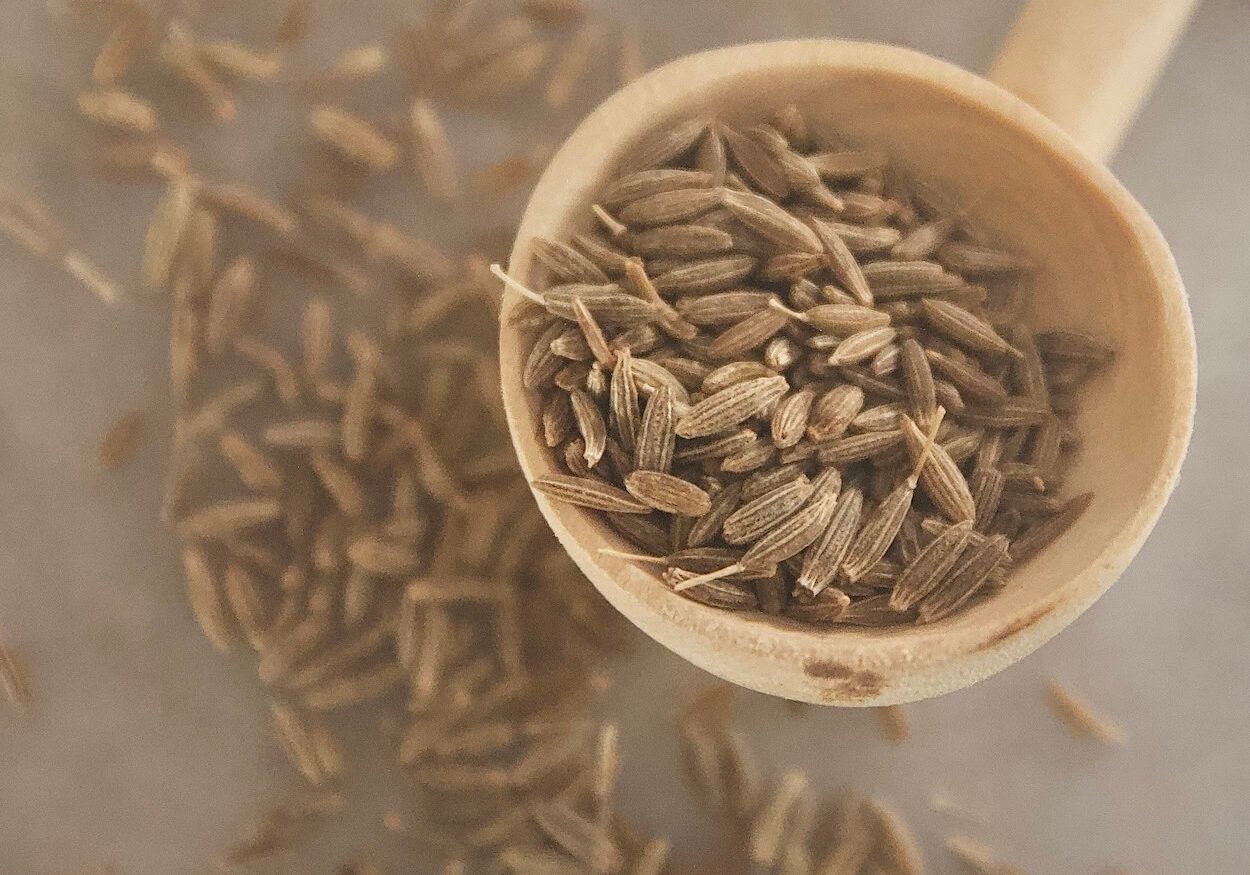 Cumin spilling out of a wooden spoon