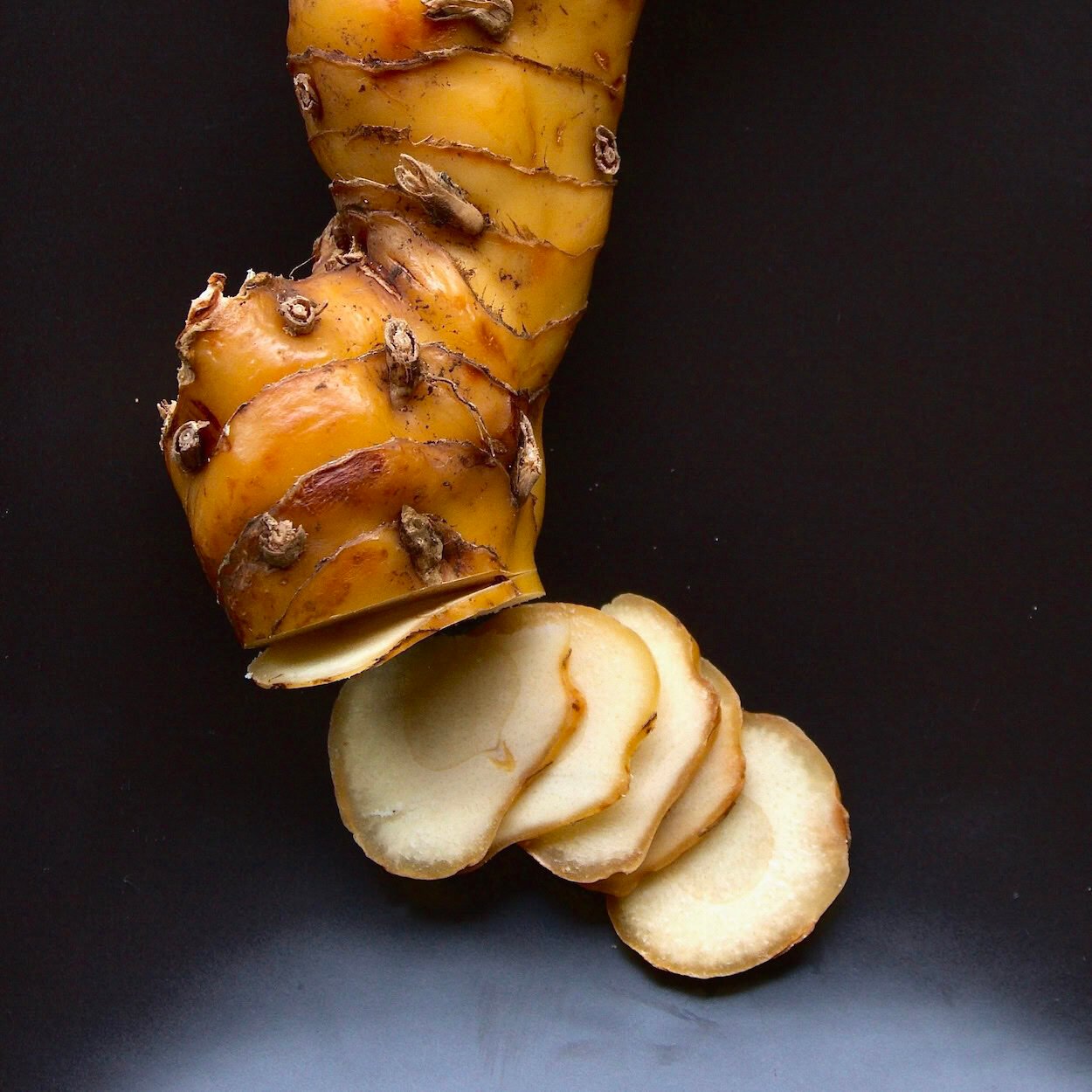 Sliced galangal rhizome on a black plate