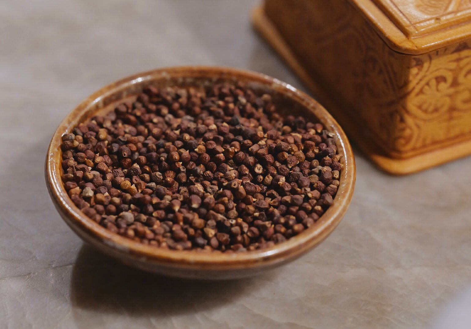 Grains of paradise seeds in ceramic bowl next to a pretty carved wood box