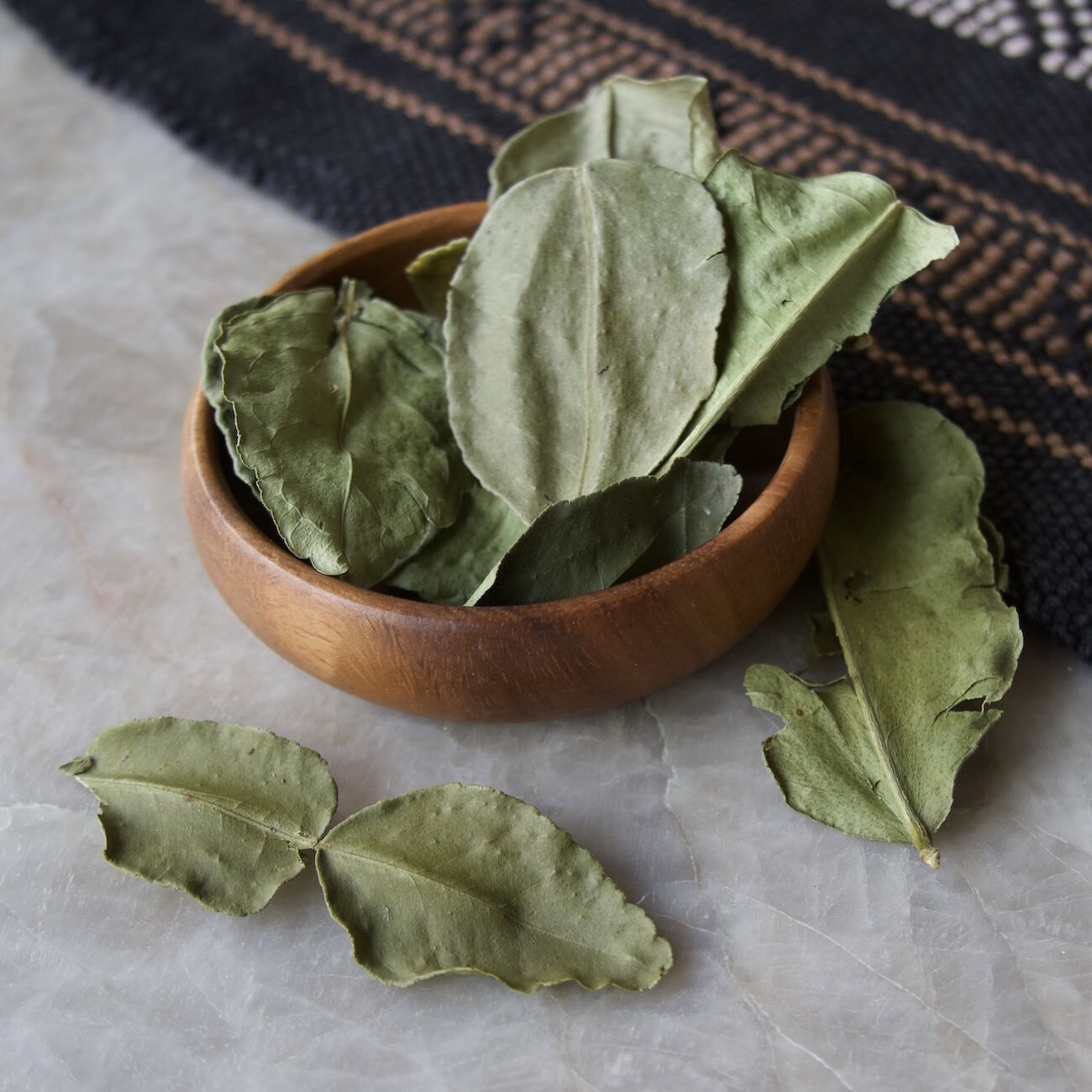 Dried makrut lime leaves in wooden bowl