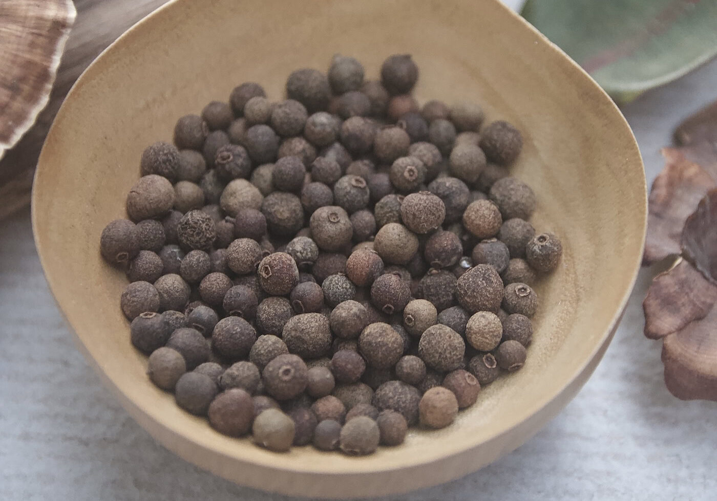 A wooden bowl filled with dried whole allspice berries